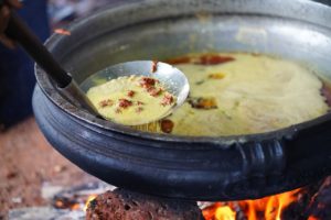 Indian soup cooking in a pan that is over a fire on the side of the street.